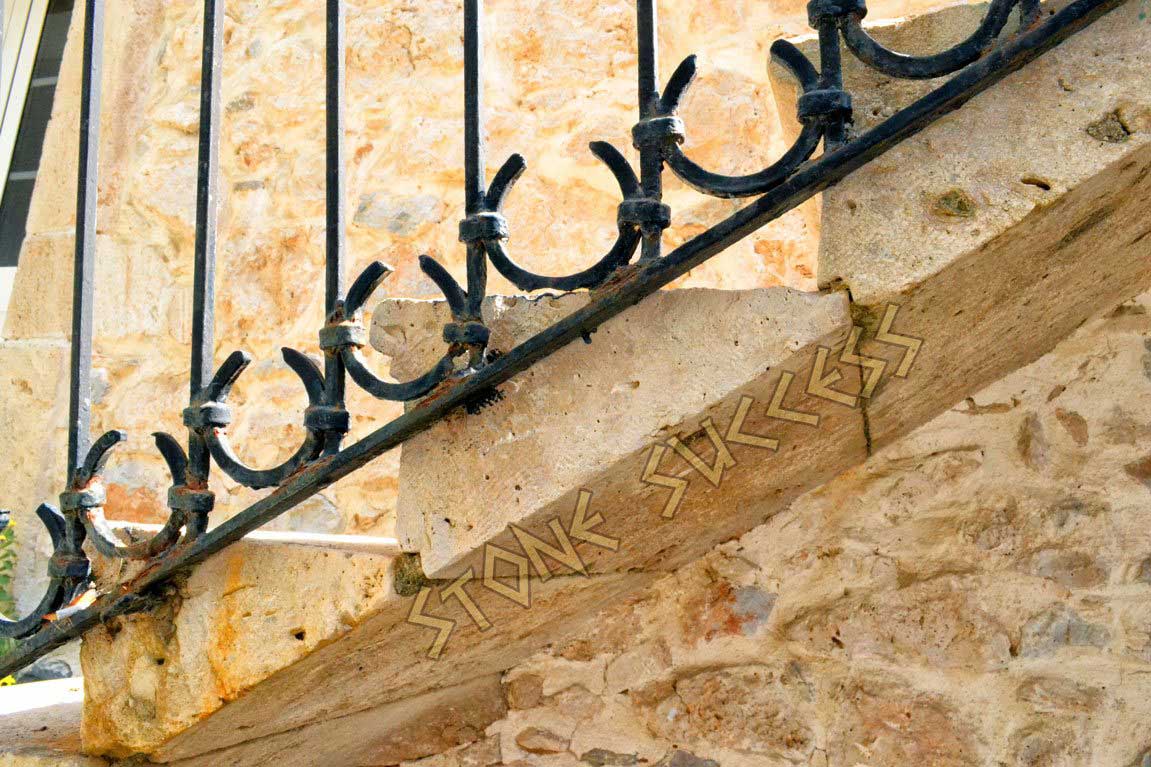 винтовая лестница из природного камня с коваными перилами